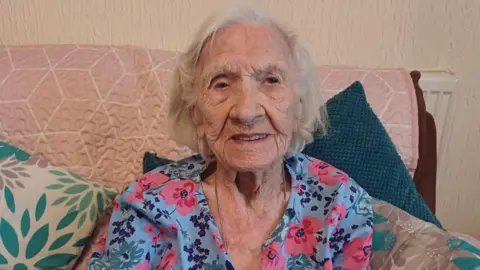 100 year old Betty Atkins sits on a sofa at her home in Paulsgrove 