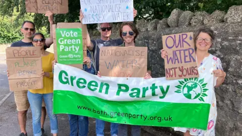 Six people stand with placards that read 'people, planet before profit', 'our water not yours', and 'nationalise water now'.