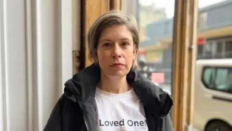 A female care home campaigner is pictured outside Huddersfield Care Home. She is wearing a black jacket and a white t shirt with a picture of her Mum, Janet on. 