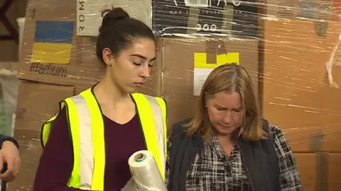 Two women in a warehouse bowing their heads