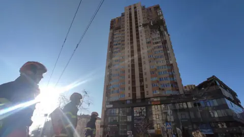 Anadolu Agency / Getty Images First responders are seen near an apartment building damaged by recent shelling in Kyiv, Ukraine February 26, 2022.