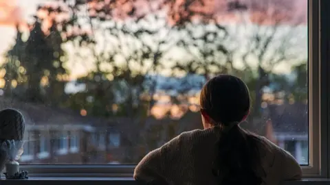 Getty Images A girl looks out of a window at a sunset