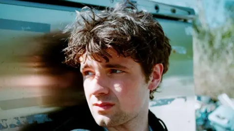 Ben Andrew A picture of Charlie stood in front of a metal wall. He has brown hair and a short beard.