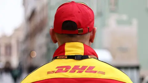 Male DHL worker in yellow and red branded jacket wearing a red cap