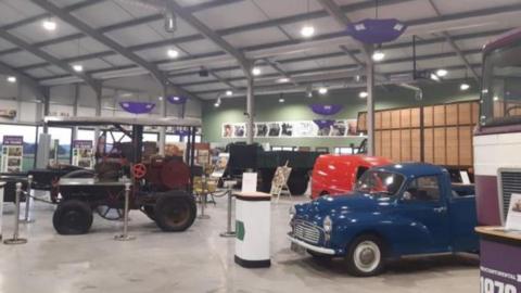 A warehouse building with old cars and vans from various decades 