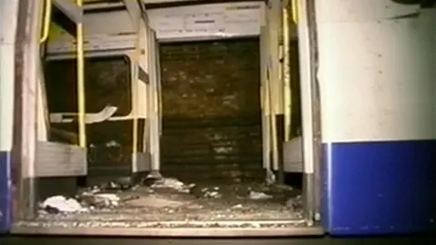 PA Media A white and blue tube carriage. The doors are open and debris from the explosion can be seen on the floor. Bricks from the London Underground wall can be seen through the opposite doors of the carriage. It is dark and the photo has been taken with a flash.