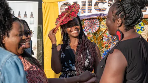 Mark McNulty A woman holds her hat in the sunshine as she smiles in the festival sunshine