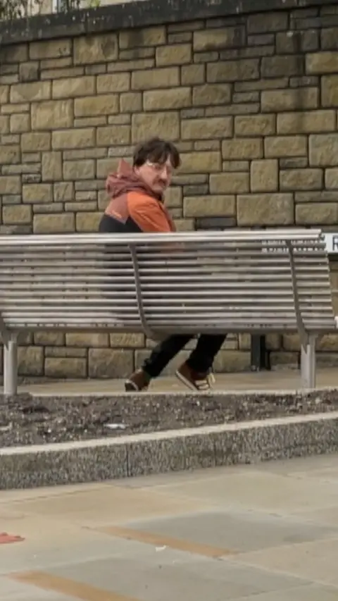 A man on a bench facing a wall
