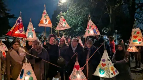 A group of people in a park carrying colourful lanterns as part of Bradford's First Festival of the Dead