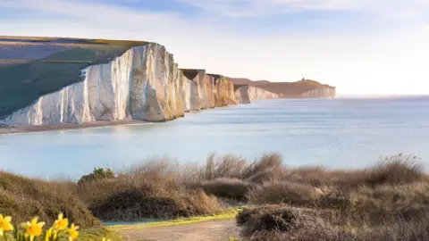 The images shows white cliffs facing the ocean with a blue sky in the background.