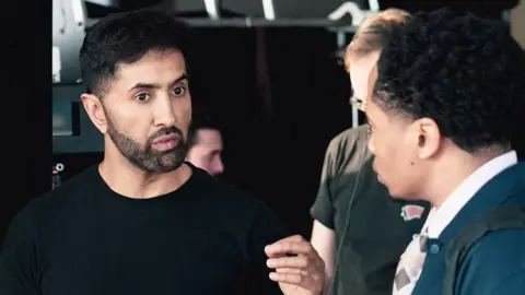 Amar Singh Sethi Amar Singh Sethi directing an actor on a film set. He has short, dark hair and a dark, close cut beard. He wears a black t-shirt.