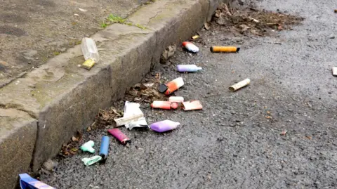 Getty Images Numerous disposable vapes are lying broken, damaged and used on the side of a pavement and street.