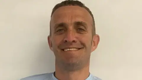 Hope Housing A man with short brown hair smiles at the camera standing against a white wall