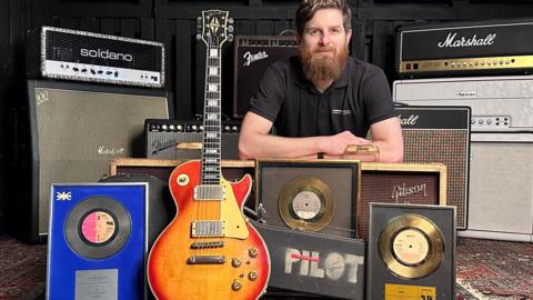Auctioneer Luke Hobbs surrounded by amps, framed discs and the guitar