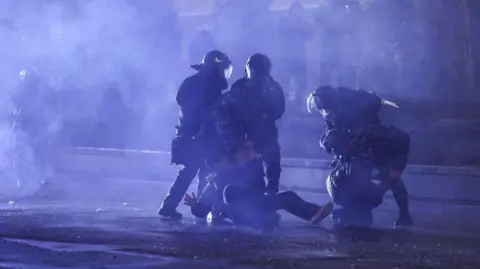 Getty Images Police escort a protester in Georgia down a dark street in the capital