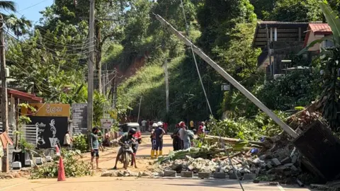 Irie Perera A group of people looking at some rubble and a pole that has toppled over