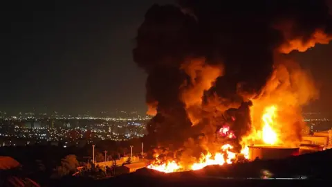 Getty Images Fire and smoke rise into the sky after an Israeli attack on the Shahran oil depot on June 15