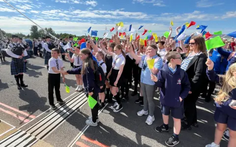 Children waving flags in the middle of a bridge. Two children are shaking hands