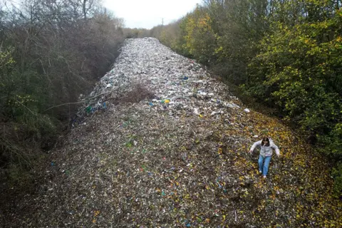An aerial photograph shows environmental campaigners filming content for social media on a large pile of fly-tipped waste, dumped in a field between the River Cherwell and the A34 near Kidlington, Oxfordshire, west of London on November 16, 2025.