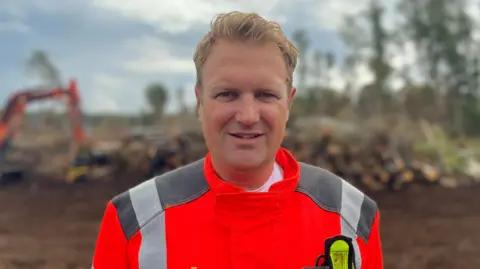 Stuart Smith - a man with short blonde hair, wearing a bright orange-coloured jacket, smiling for the camera.