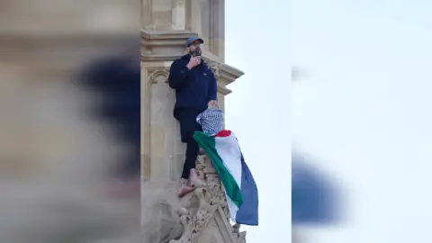 PA Media A man with a Palestine flag speaks into a phone as he stands on the Elizabeth Tower