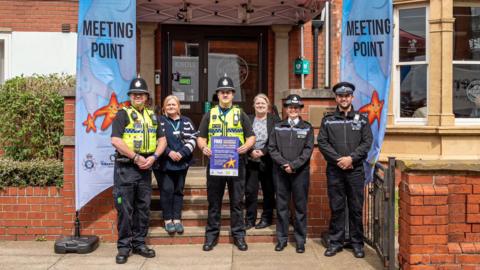 A team of police officers stand with banners and posters
