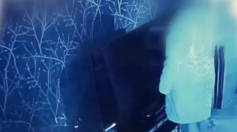 An inside wall that is blue and white. A woman whose face is not visible is standing in front of the wall, which has a TV in front of it.