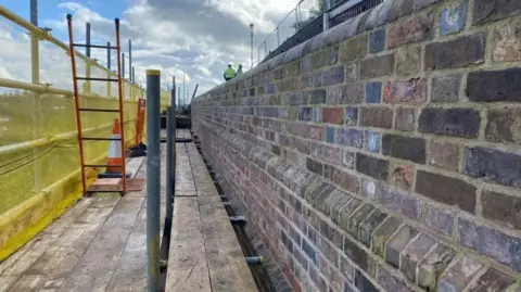 Bridgnorth Town Council A brick wall with a wooden walkway alongside and yellow netting to the left hand side.