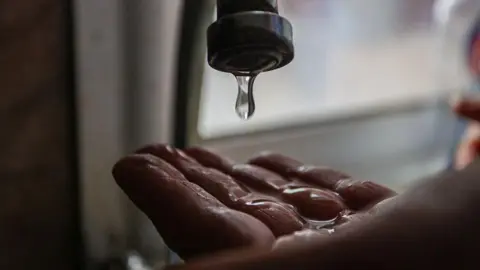 Getty Images Water drips from a tap onto someone's hand. 