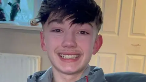 Christopher McBurnie, a teenager with short dark hair and a long fringe, smiling.