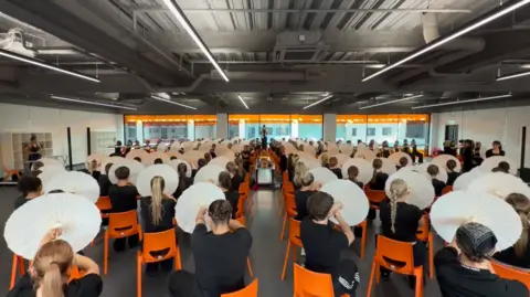 LMA Universty The LMA group in a training session using white paper parasols and sitting on orange chairs in a large room