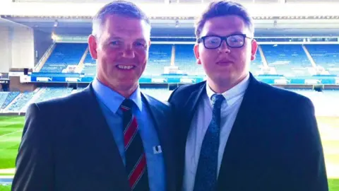 BHF Scotland Two men wearing suits with shirts and ties standing in front of the stands at Ibrox stadium