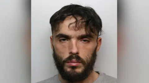 The mugshot of Matthew Haylett, who has short black hair and a black beard.