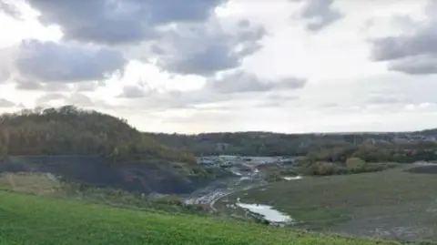 a grassy field overlooking a dirt road into a valley with what looks like a quarry