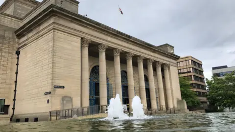 Sheffield city hall is a light stone building with several large pillars and a fountain in front