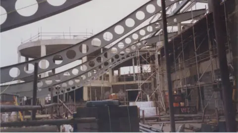 An image from the exhibition of Rugby Art Gallery and Museum under construction. Concrete, scaffolding and steel beams have been put into place with building supplies around the site. 