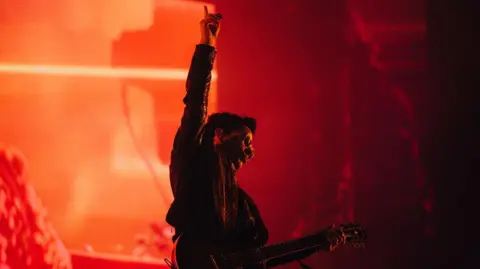 PA Kelly Jones holds an arm aloft, pointing to the sky, as he performs on stage.