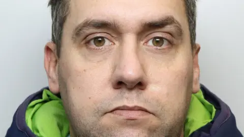 West Yorkshire Police A mugshot of Walsh, who is photographed from the front against a plain light background. He is wearing a dark padded jacket with a bright green inner lining visible around the collar. His hair is short and neatly styled, and the ears are visible on both sides.