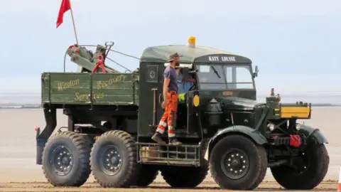 Burnham-on-Sea.com A large truck with six wheels is pictured, with a man hanging off the side of it.