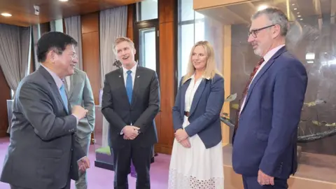Lin Chia-lung smiling as he speaks to four other New Zealand representatives. They are standing in a small circle and dressed in formal attire.