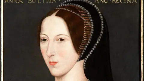 A portrait of Anne Boleyn where she is wearing black robes. She has a necklace on with the letter B as the pendant and her hands are visible holding a red rose.