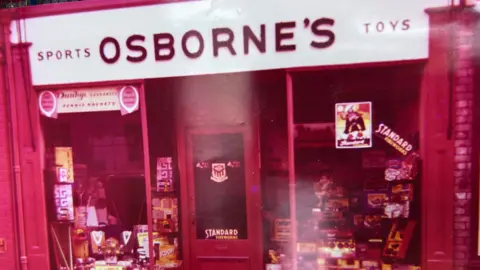 Will Osborne A photo of a toy shop with a red tint. A large white sign reading "Sports, Osborne's toys" is above the entrance.