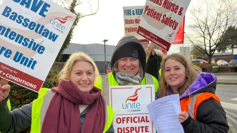 Three women holding signs supporting strike action over rotation plans at Bassetlaw Hospital and Doncaster Royal Infirmary.
