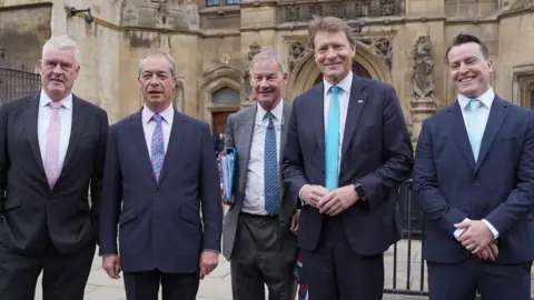 PA Media Reform UK MPs Lee Anderson, Nigel Farage, Rupert Lowe, Richard Tice and James McMurdock arrive at the House of Commons. They are in a row wearing suits and ties of various hues.