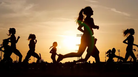 Silhouette of a group of women running in front of the sun at a low angle on the horizon 