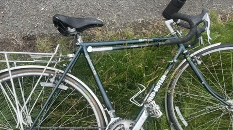 Police Scotland A green racing bike with black saddled and handlebars lies on its side in grass at the side of a road