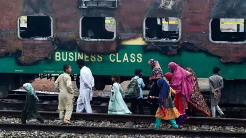 Getty Images A family walks passed the charred remains of a train carriage