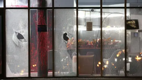 Palestine Action Large window panels have been smashed. The office on the other side of the glass panels is covered in sprayed red paint