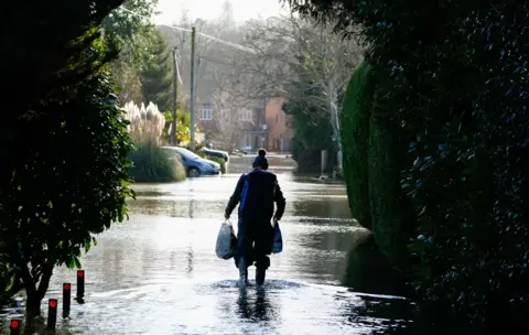 PA Media A man walks through floodwaters