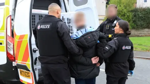 Photograph of officers from Operation Vulcan arresting a man in the Brinnington area of Stockport. The image shows three police officers and one suspect.